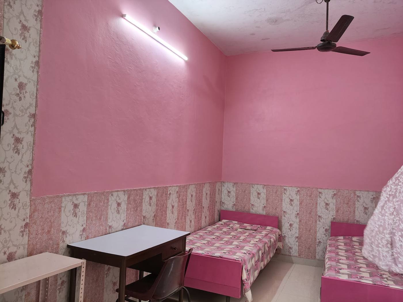 Pink room with beds, a study table and a ceiling fan